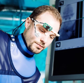 Ein Mann in Schutzkleidung hat eine technische Apparatur für ein Experiment auf dem Kopf.