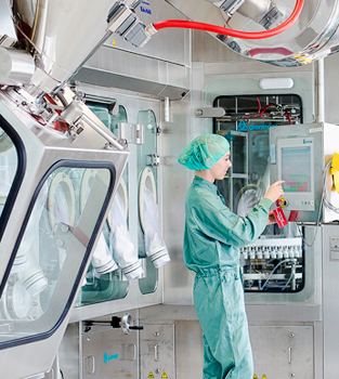 Eine Frau in steriler Schutzkleidung bedient das Touchpad einer Maschine in einem Labor.